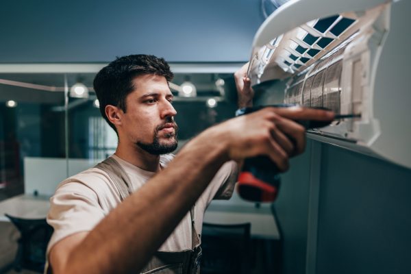 A technician is focused on installing an air conditioning unit in a contemporary office, using a screwdriver and ensuring everything is functioning properly. The time is afternoon.